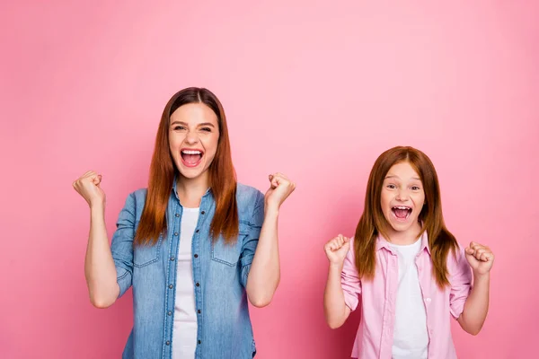 Retrato de señoras alegres con el pelo largo levantando puños gritando sí usando jeans camisas de mezclilla aisladas sobre fondo rosa — Foto de Stock