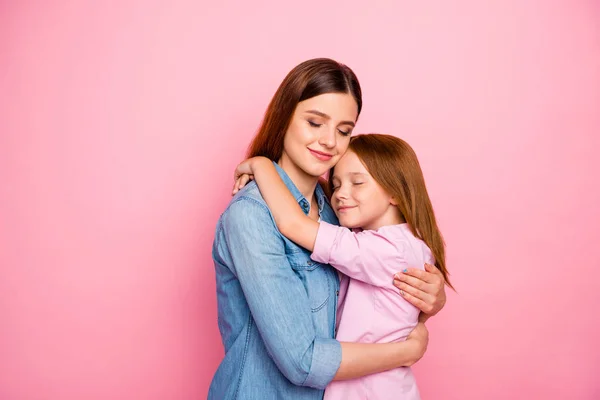 Portrait of relaxed lady hugging her daughter closing eyes wearing denim jeans shirt isolated over pink background — Stock Photo, Image