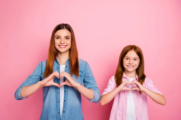 Porträtt av charmiga flickor med långt hår gör hjärta bär denim jeans skjorta isolerad över rosa bakgrund — Stockfoto