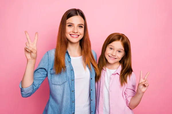 Porträtt av glada tjejer med långt hår gör v-skyltar klädd i jeans jeans skjortor isolerade över rosa bakgrund — Stockfoto