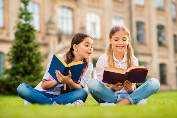 Portrett av to pene, vakre, muntre, intelligente jenter som sitter i grønt gress. Frisk luft og leser lekser utendørs. – stockfoto