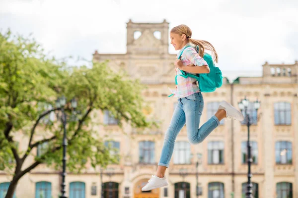 Foto em tamanho real de menina alegre com mochila mochila correndo para a academia vestindo xadrez xadrez t-shirt jeans jeans ao ar livre — Fotografia de Stock