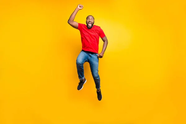 Полноразмерное фото прыгуна в джинсах в красной футболке, радующегося своей победе в чем-то изолированном на жёлтом фоне — стоковое фото