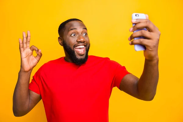 Foto van funky grappig model zwarte man nemen selfie dragen rode t-shirt tonen OK oke symbool terwijl geïsoleerd met gele achtergrond — Stockfoto