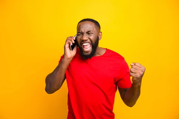 Foto de homem negro exultante sabendo que ele se tornou vencedor de algo tão regozijante desfrutando de informações de notícias enquanto isolado com fundo amarelo — Fotografia de Stock