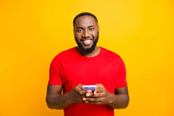 Sarı arka plan ile izole ederken kamera gülümseyen iki eliyle telefonunu tutan basit iyi sevimli yakışıklı siyah adam Fotoğraf — Stok fotoğraf