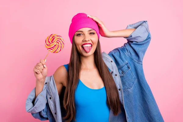 Retrato de senhora alegre em boné mostrando sua língua segurando doces usando roupa de banho isolada sobre fundo rosa — Fotografia de Stock