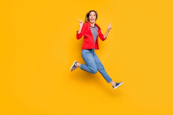 Foto de cuerpo completo de chica encantadora saltando haciendo v-signo de usar camisa de rayas rojas chaqueta vaqueros aislados sobre fondo amarillo — Foto de Stock