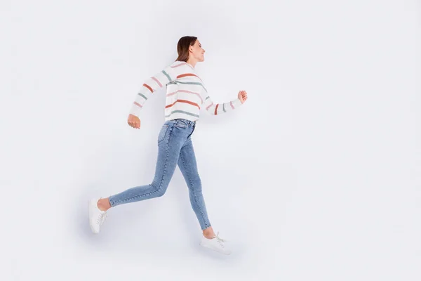 Полноразмерное фото симпатичного человека, бегущего с сияющей улыбкой в джинсах в полосатом свитере на белом фоне — стоковое фото