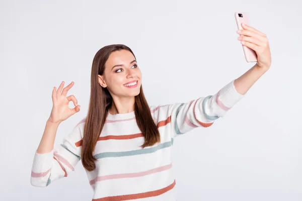 Όμορφη κυρία κάνοντας selfie σε νέο τηλέφωνο δείχνει εντάξει σύμβολο φθορά ριγέ πουλόβερ απομονωμένο λευκό φόντο — Φωτογραφία Αρχείου