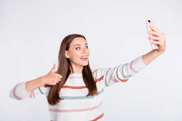 Красива дама робить селфі на новому телефоні, піднімаючи великий палець вгору в смугастій пуловері ізольований білий фон — стокове фото