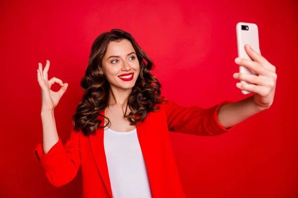 Портрет очаровательной женщины, делающей селфи с современной технологией носить пиджак изолирован на красном фоне — стоковое фото