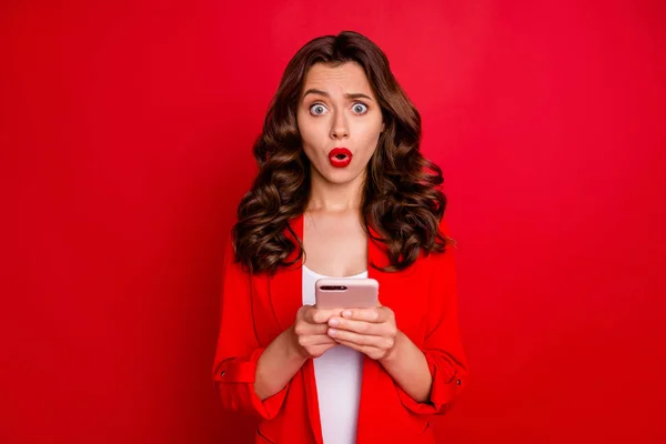 Portret van onder de indruk dame met heldere pommade schreeuwen OMG lezing nieuws op haar mobiele telefoon dragen moderne jas geïsoleerd over rode achtergrond — Stockfoto