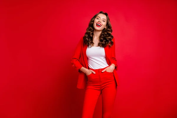 Портрет веселої леді, яка сміється, кладе руки в кишені в сучасному костюмі ізольовані на червоному тлі — стокове фото