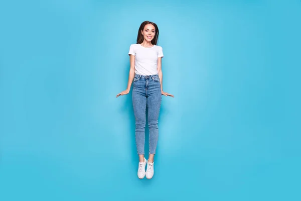 Foto de longitud completa de la juventud bonita saltando en movimiento con pantalones vaqueros camiseta blanca de mezclilla aislado sobre fondo azul — Foto de Stock