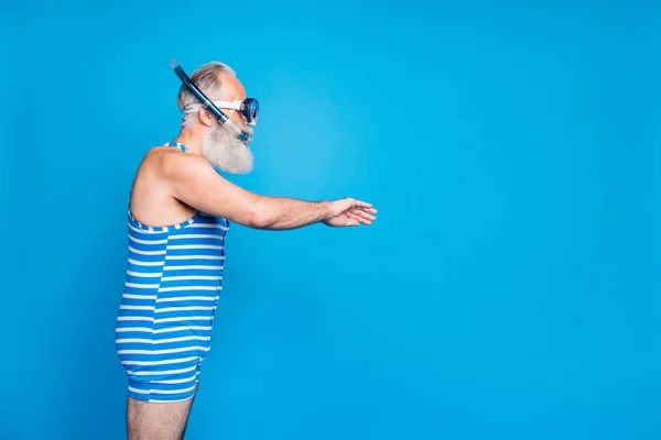 Foto de perfil de un hombre retirado enfocado moviendo la braza usando equipo de snorkel usando trajes de baño a rayas aislados sobre fondo azul — Foto de Stock