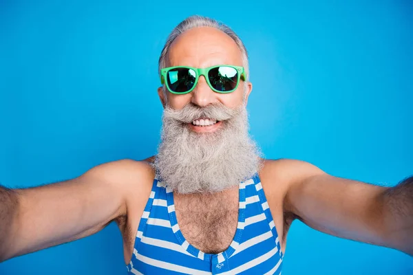 Близкое фото веселого мужчины, делающего селфи с зубастой улыбкой в очках в полосатых очках купальный костюм изолирован на синем фоне — стоковое фото