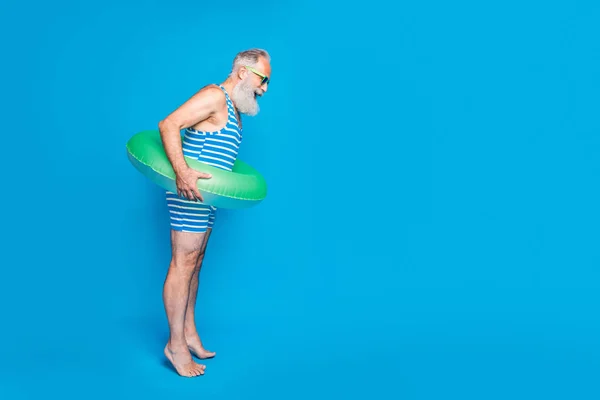 Ganzkörperprofil Seite Foto des überraschten Mannes Blick nach unten mit seiner Brille halten grünen Lebensretter tragen gestreiften Badeanzug isoliert über blauem Hintergrund — Stockfoto