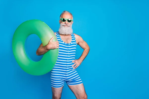 파란색 배경 위에 고립 된 줄무늬 수영복을 입고 녹색 장난감 원을 들고 안경 안경에 자신감있는 남자의 초상화 — 스톡 사진