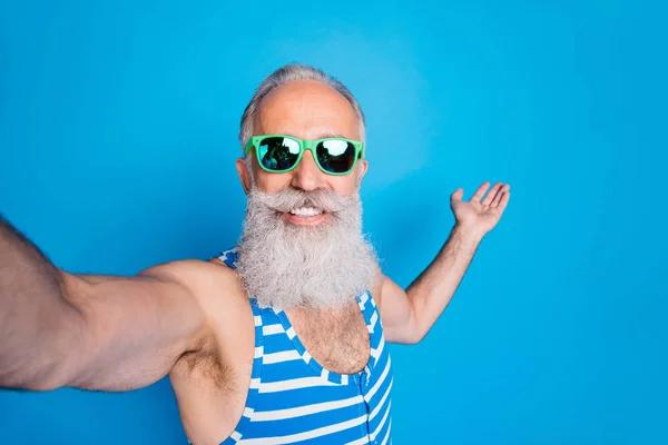 Foto de cerca del hombre retirado en gafas gafas que sostienen su palma haciendo selfie usando ropa de baño a rayas aisladas sobre fondo azul — Foto de Stock