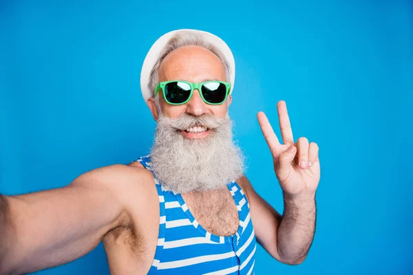 Κλείστε τη φωτογραφία του εύθυμου παππού με γυαλιά γυαλιών κάνοντας selfie v-πινακίδες φορώντας καπάκι καπέλο ριγέ μαγιό sunhat Παναμά απομονωμένη πάνω από μπλε φόντο — Φωτογραφία Αρχείου