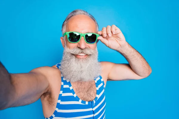 Foto de cerca de una persona jubilada tocando sus anteojos haciendo fotos usando trajes de baño a rayas aislados sobre fondo azul —  Fotos de Stock