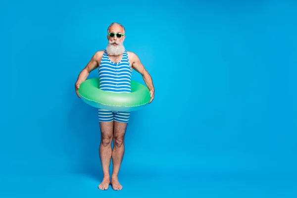 Teljes test fénykép benyomást nyugdíjas a szemüveges szemüveges gazdaságban gumi gyűrűt viselő csíkos fürdőruhát izolált kék háttér — Stock Fotó