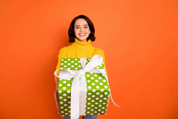 Foto av glad trevlig tjej klädd i Jeans denim Gifting något till dig medan isolerad med orange bakgrund — Stockfoto