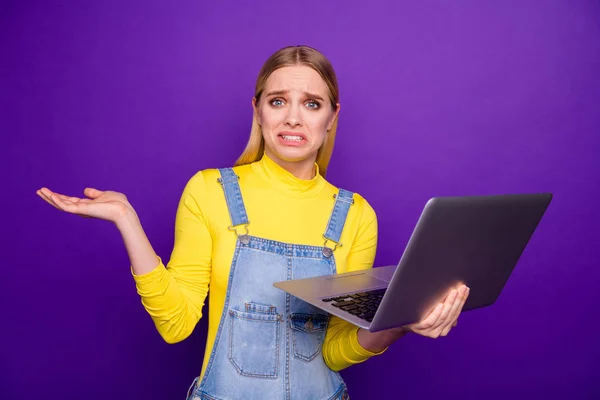 Retrato de jovens desapontados segurando tecnologia moderna vestindo jeans jeans jeans de gola alta amarelo em geral isolado sobre fundo violeta roxo — Fotografia de Stock