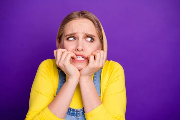 Foto de cerca de la juventud frustrada mordiéndose las uñas mirando con pantalones vaqueros de cuello alto amarillos sobretodo aislados sobre fondo violeta —  Fotos de Stock