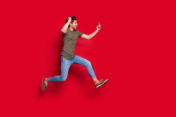 Volledige grootte profielfoto van cool Guy Jumping hoge maken selfies dragen casual outfit geïsoleerd op rode achtergrond — Stockfoto