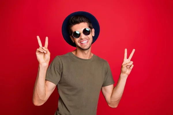 Foto del viajero mostrando las manos v-sign wear vintage hat sun specs and grey t-shirt isolated on red background — Foto de Stock