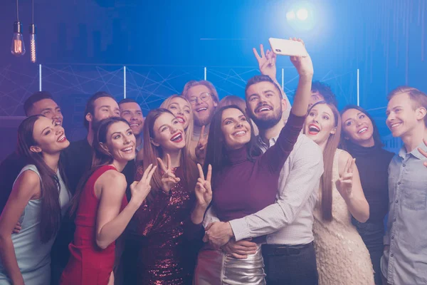 Portrait of nice well-dressed chic glamorous attractive fashionable stylish gorgeous cheerful positive glad ladies and guys having fun taking selfie showing v-sign symbol at luxury fogged nightclub