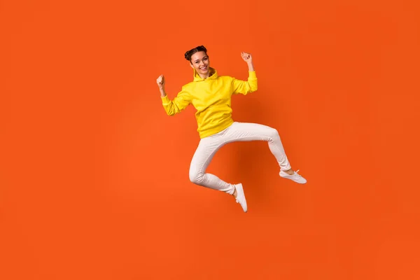 Foto full size di allegro salto millenario con le braccia alzate indossando pantaloni pantaloni isolati su sfondo arancione — Foto Stock