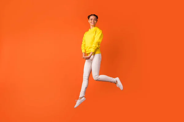 Foto de tamaño completo de bastante adolescente saltando buscando tienen sonrisa en su cara aislada sobre fondo naranja — Foto de Stock