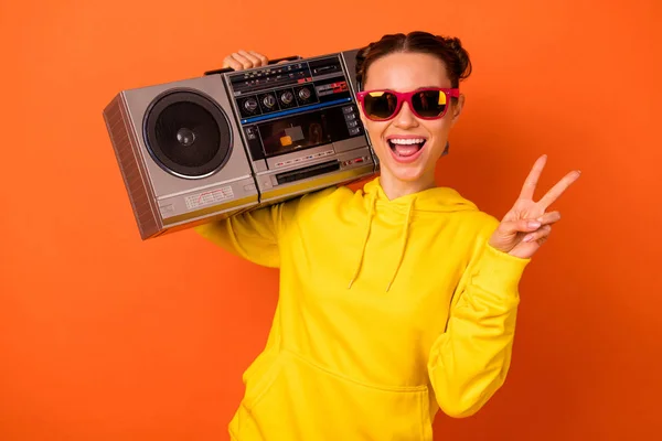 Portret van opgewonden meisje met top-Knot maken v-Signs houden Boombox geïsoleerd over oranje achtergrond — Stockfoto