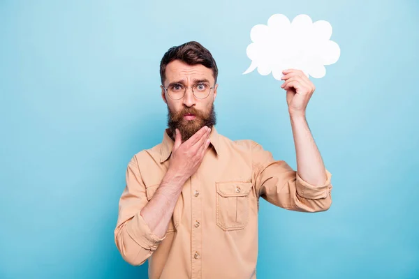 Retrato del hombre de mente en gafas con gafas que sostienen la burbuja de la tarjeta de papel tocando su barbilla con camisa marrón aislada sobre fondo azul — Foto de Stock