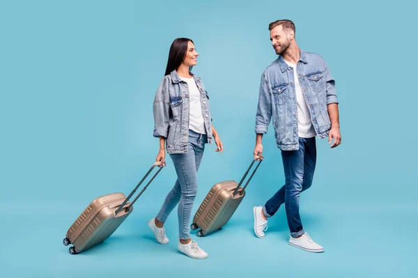 Foto lateral de perfil de tamaño completo de dos novios que llevan equipaje despedido usando chaquetas vaqueras aisladas sobre fondo azul — Foto de Stock