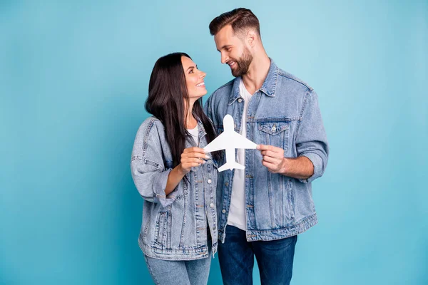 Photo of fascinating beautiful nice cute couple of bride and groom wearing denim jackets holding small airplane before going abroad while isolated with blue background