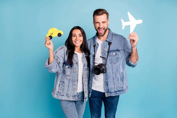 Retrato de gente casada alegre sosteniendo el avión blanco amarillo de la tarjeta de papel y la cámara del taxi usando chaquetas vaqueras aisladas sobre fondo azul — Foto de Stock