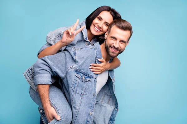 Portrait of cute man carrying his sweetheart making v-signs wearing denim jeans jacket isolated over blue background — Stock Photo, Image