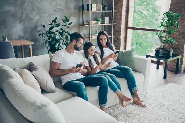 Mooi aantrekkelijk mooi vrolijk vrolijk vriendelijk schattig gezond gezin dragen casual witte t-shirts jeans zittend op de Bank met behulp van 5g app browsen op industriële loft stijl interieur woonkamer — Stockfoto