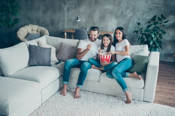 Portrait of nice attractive lovely cheerful family mommy daddy wearing casual white t-shirts jeans denim sitting on sofa enjoying video spending free time weekend at industrial style interior room — Stock Photo, Image