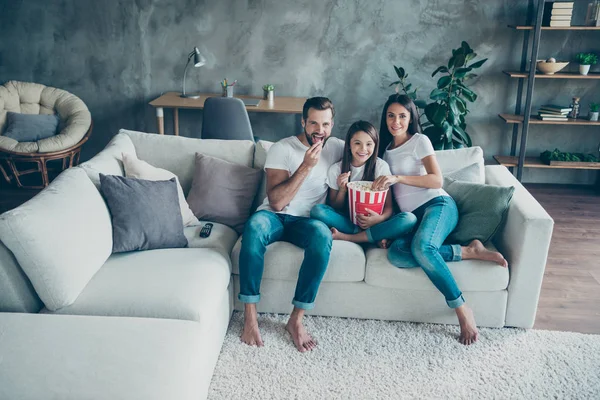 Портрет красивой привлекательной милой веселой дружелюбной идиллической семьи в джинсах в повседневных белых футболках, сидящей на диване и наслаждающейся видео отпуском в салоне промышленного стиля — стоковое фото