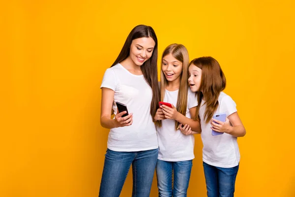 Foto de tres graciosas damas sosteniendo teléfonos viendo humor video usar ropa casual aislado fondo amarillo —  Fotos de Stock