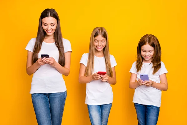 Foto de tres graciosas damas sosteniendo teléfonos en las manos usan ropa casual aislado fondo amarillo —  Fotos de Stock