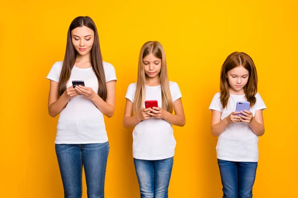 Foto de tres señoras sosteniendo teléfonos en las manos usan ropa casual aislado fondo amarillo —  Fotos de Stock