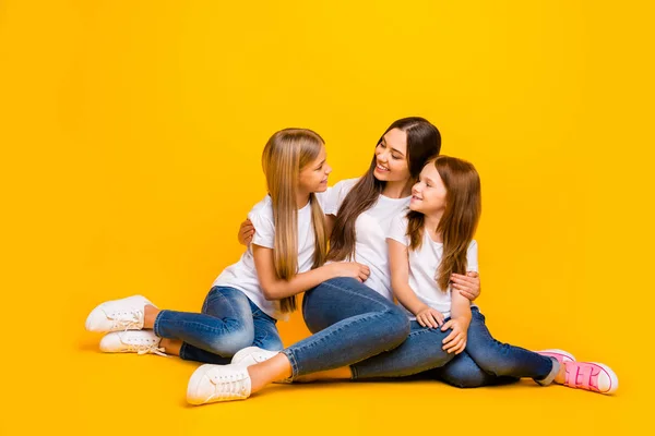 Dos damas pequeñas que se comunican con la hermosa niñera que se sienta en el suelo usan camisetas blancas casuales fondo amarillo aislado — Foto de Stock