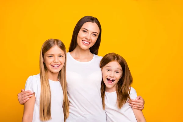 Две маленькие леди с молодой няней обнимаются носить повседневные белые футболки изолированный желтый фон — стоковое фото