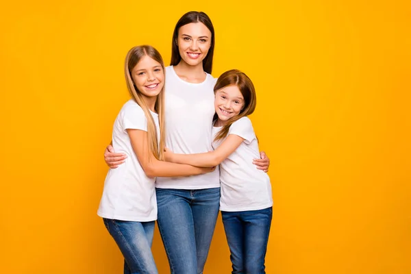 Två små damer kramar unga och vackra Babysitter slitage casual vit t-shirts isolerad gul bakgrund — Stockfoto